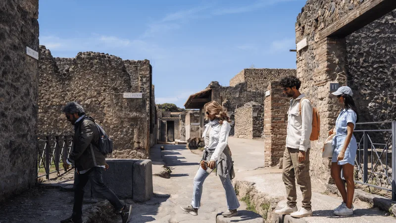 Visitors walking a stone-paved street between the house walls of Pompeii on Pompeii tours from Rome by train that end in Naples, Italy